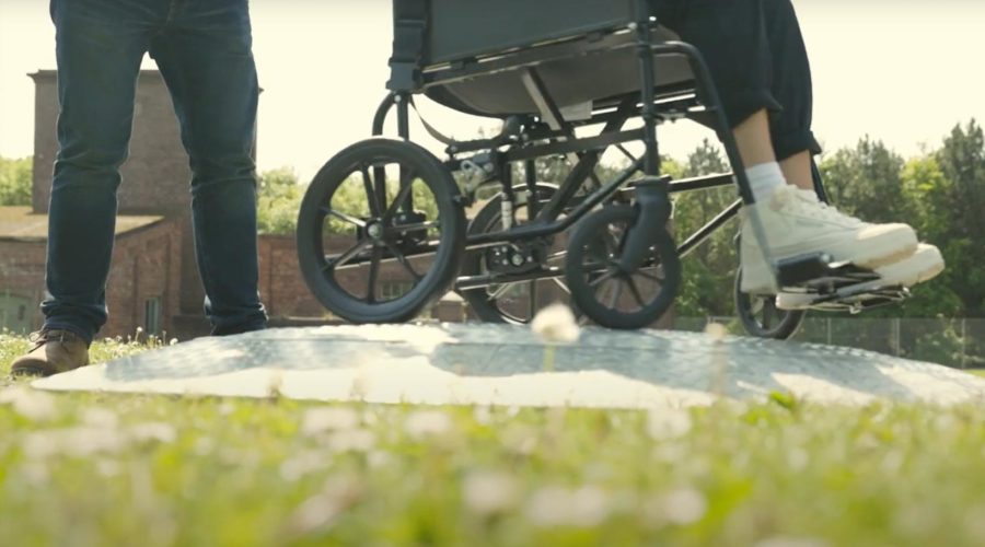 A screengrab from the video showing the bottom half of a person in wheelchair and the legs of a person behind them.